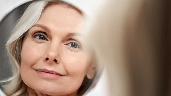 middle aged woman looking at skin in a mirror